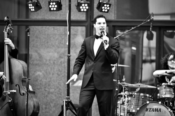 Singer holding a mic with a drumset and a cello in the background